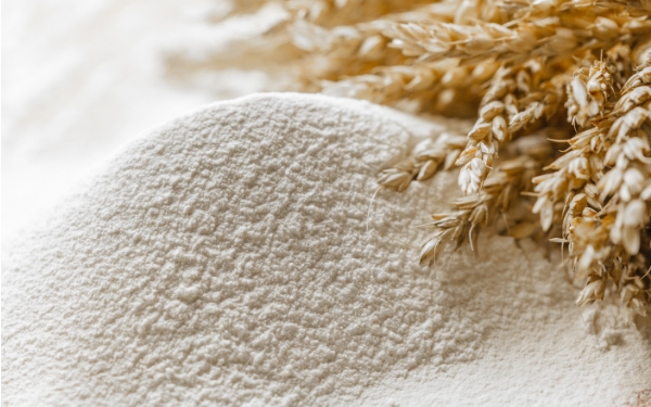 A pile of wheat flour with stalks of wheat on the right side